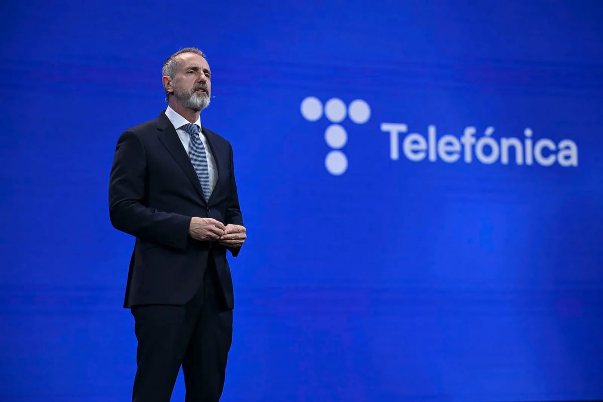 A man in a dark suit and tie stands on stage delivering a keynote speech. He has a serious and focused expression, with his hands clasped together. Behind him, a large blue screen displays the 'Telefónica' logo, indicating that the presentation is related to the telecommunications company. The setting suggests a major industry event or conference.
